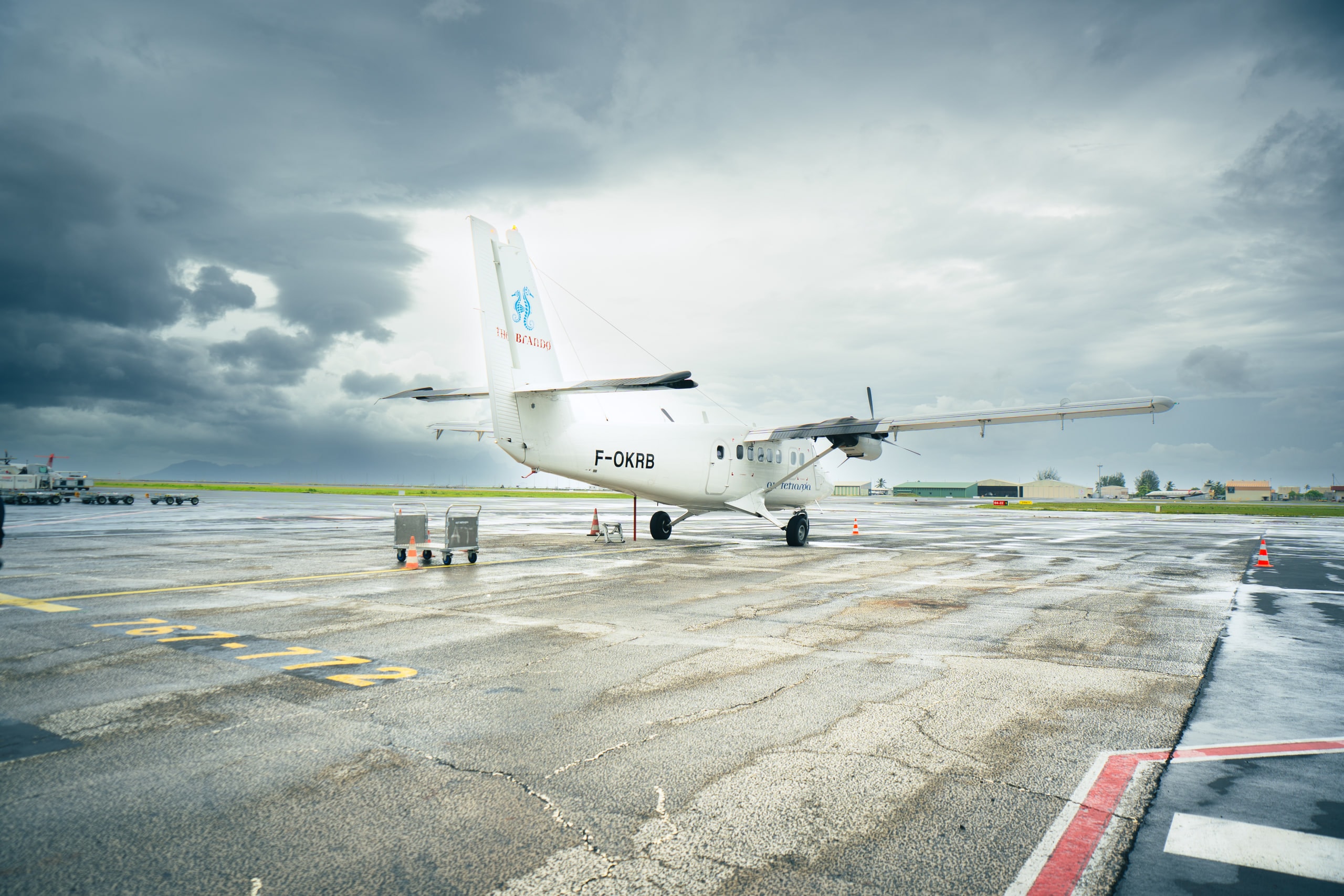 A twin propeller aircraft on a wet apron under heavy cloud