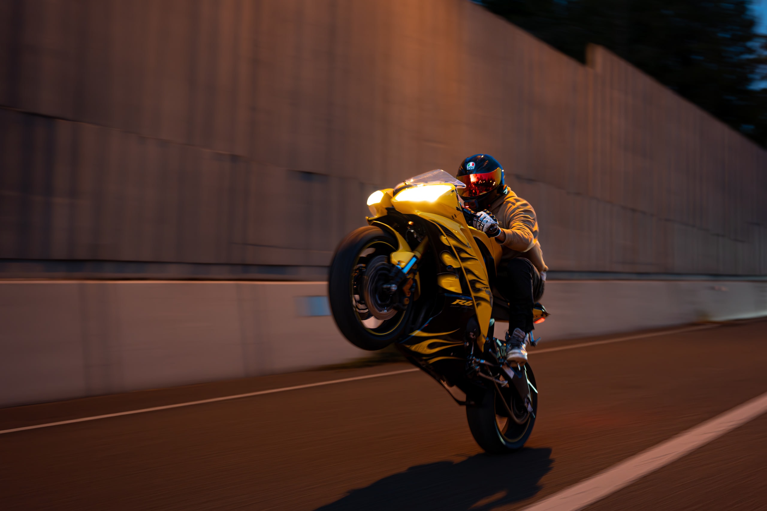 A motorcyclist pulling a wheelie along a high concrete wall