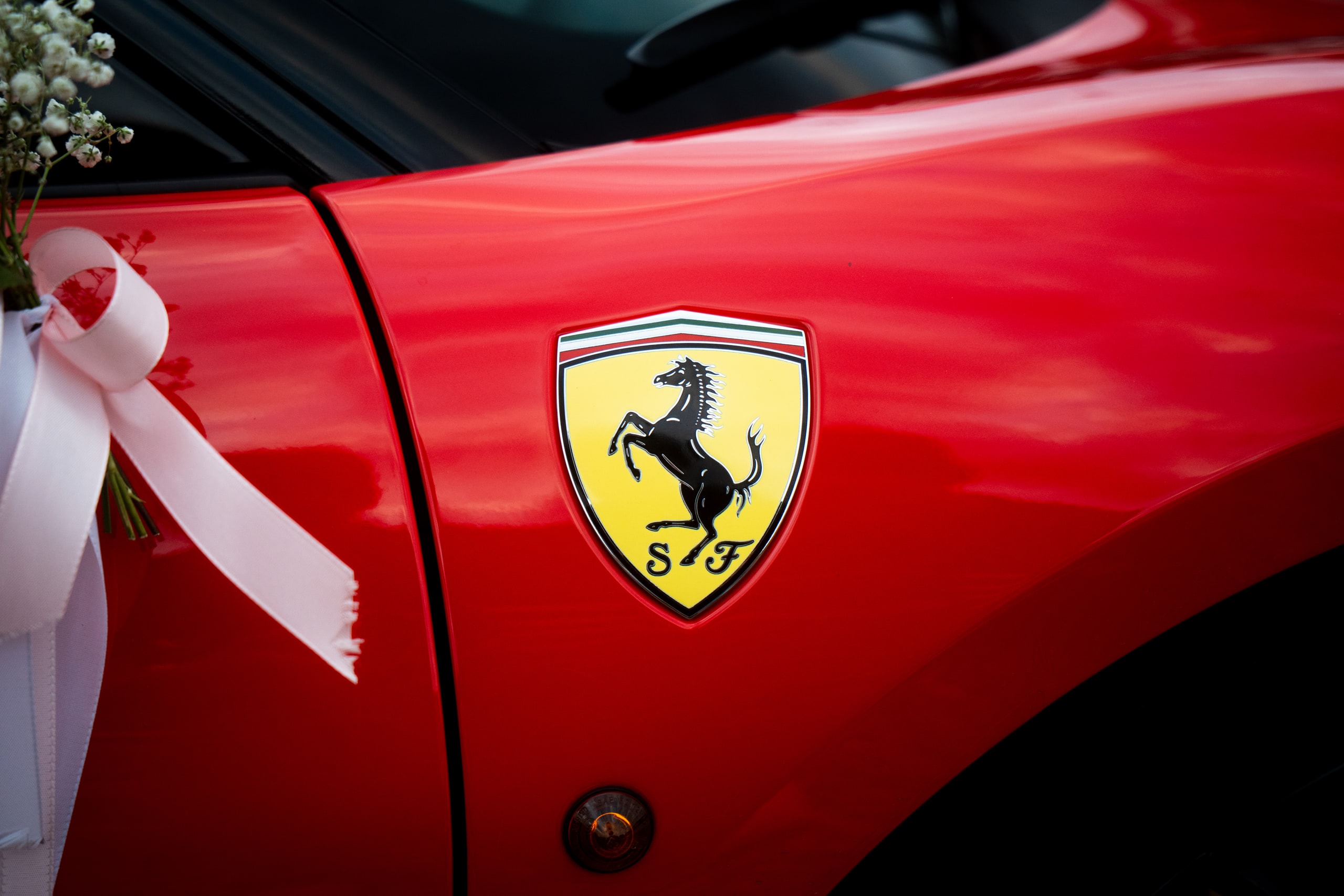 A Ferrari badge on a red wing with a white ribbon tied alongside