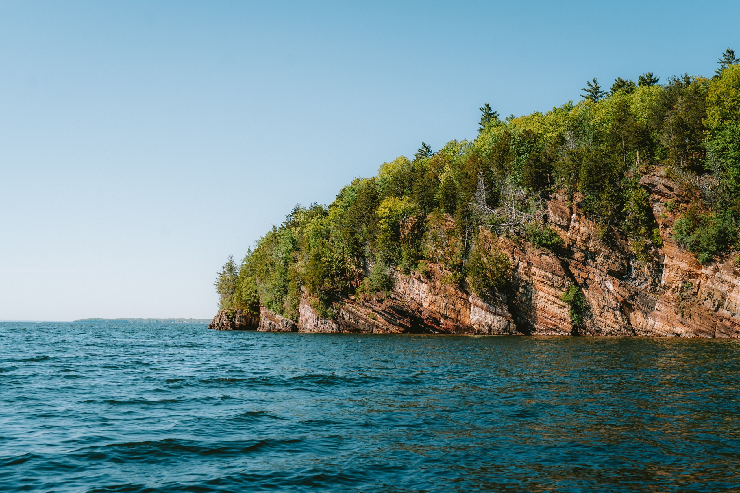 A wooded cliff dropping into deep blue water