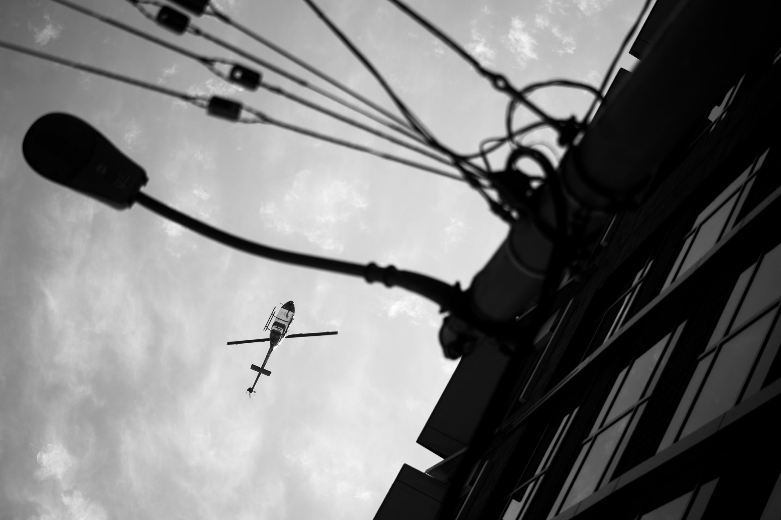 A streetlight and overhead wires with a helicopter beyond, in black and white