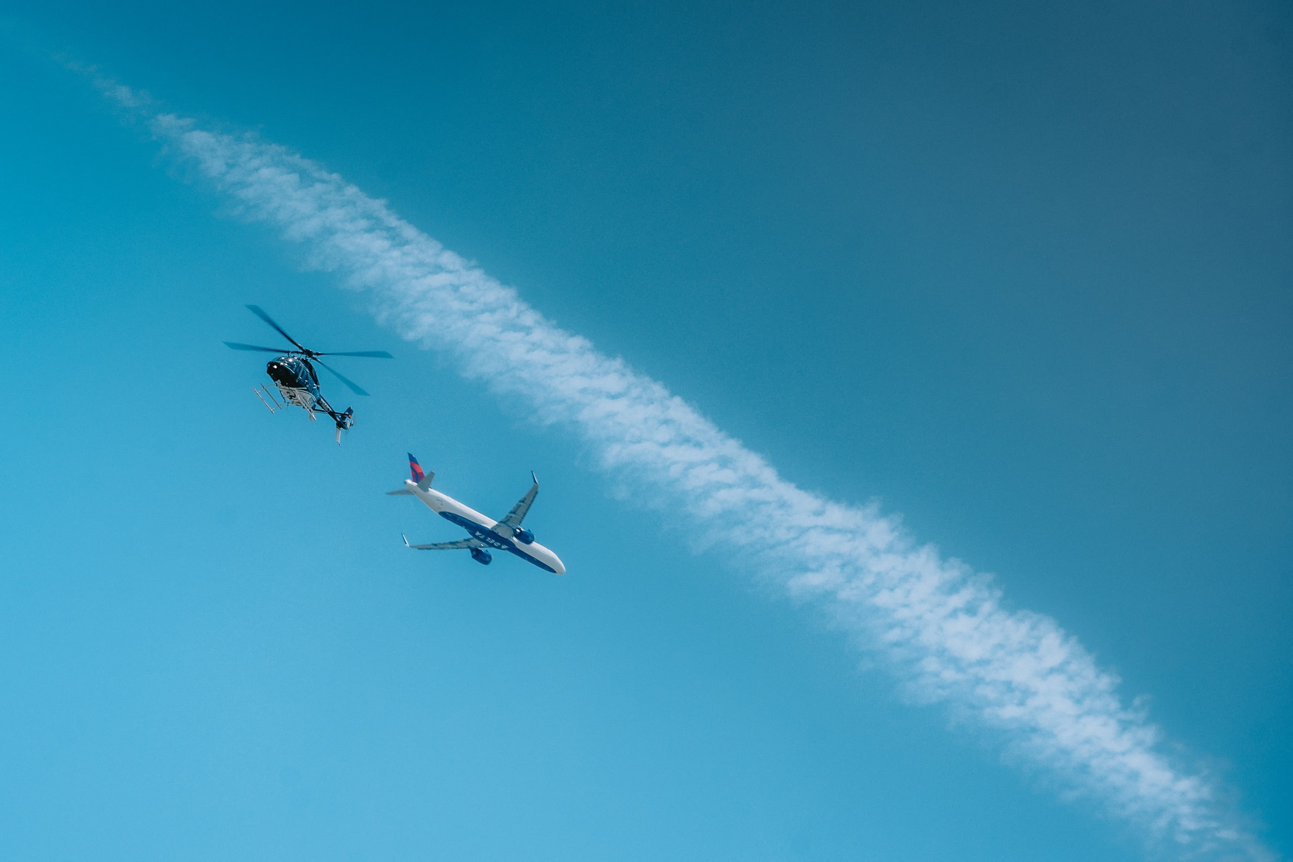 A helicopter and an airliner crossing beneath a contrail