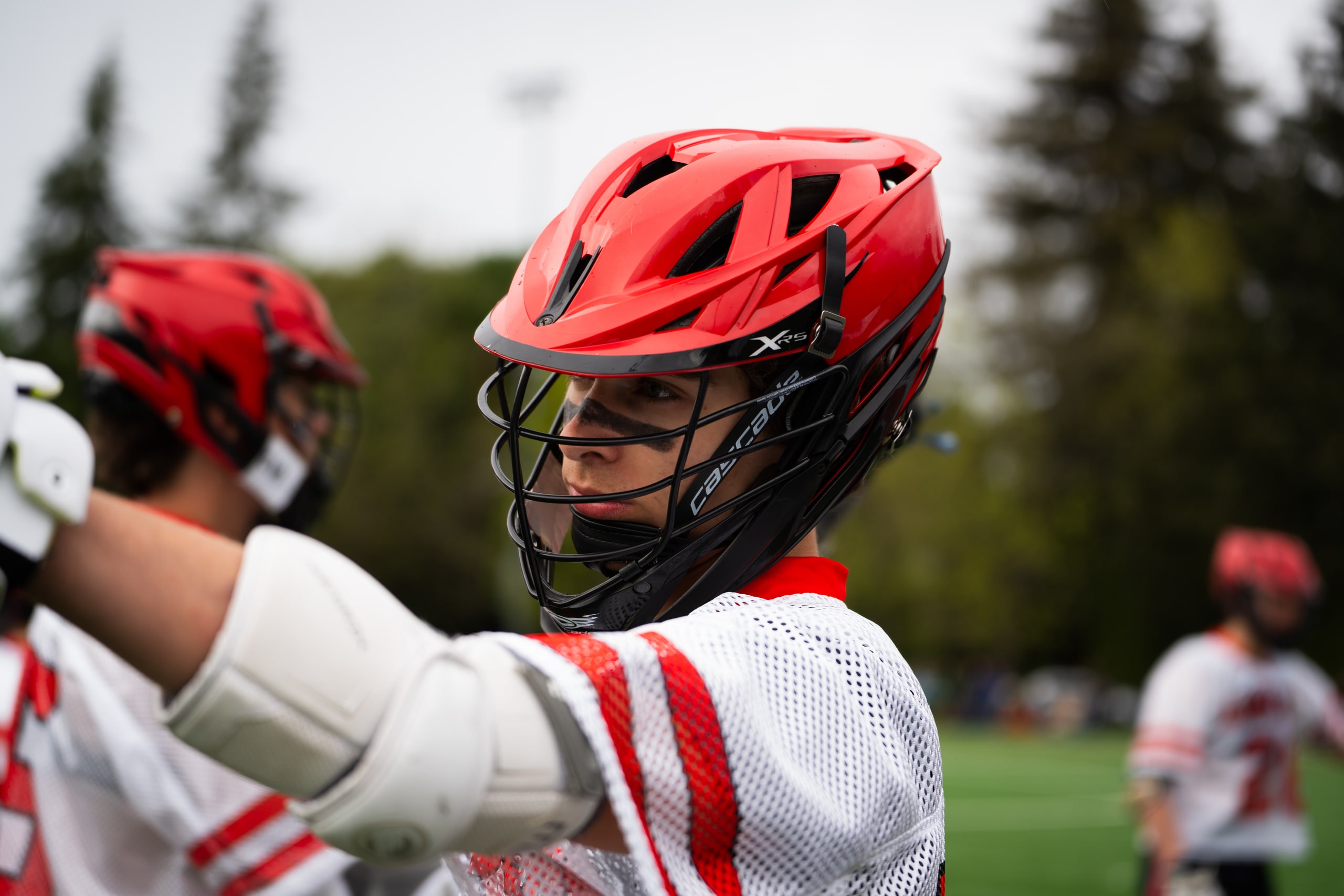 A lacrosse player in a red helmet raising a gloved hand