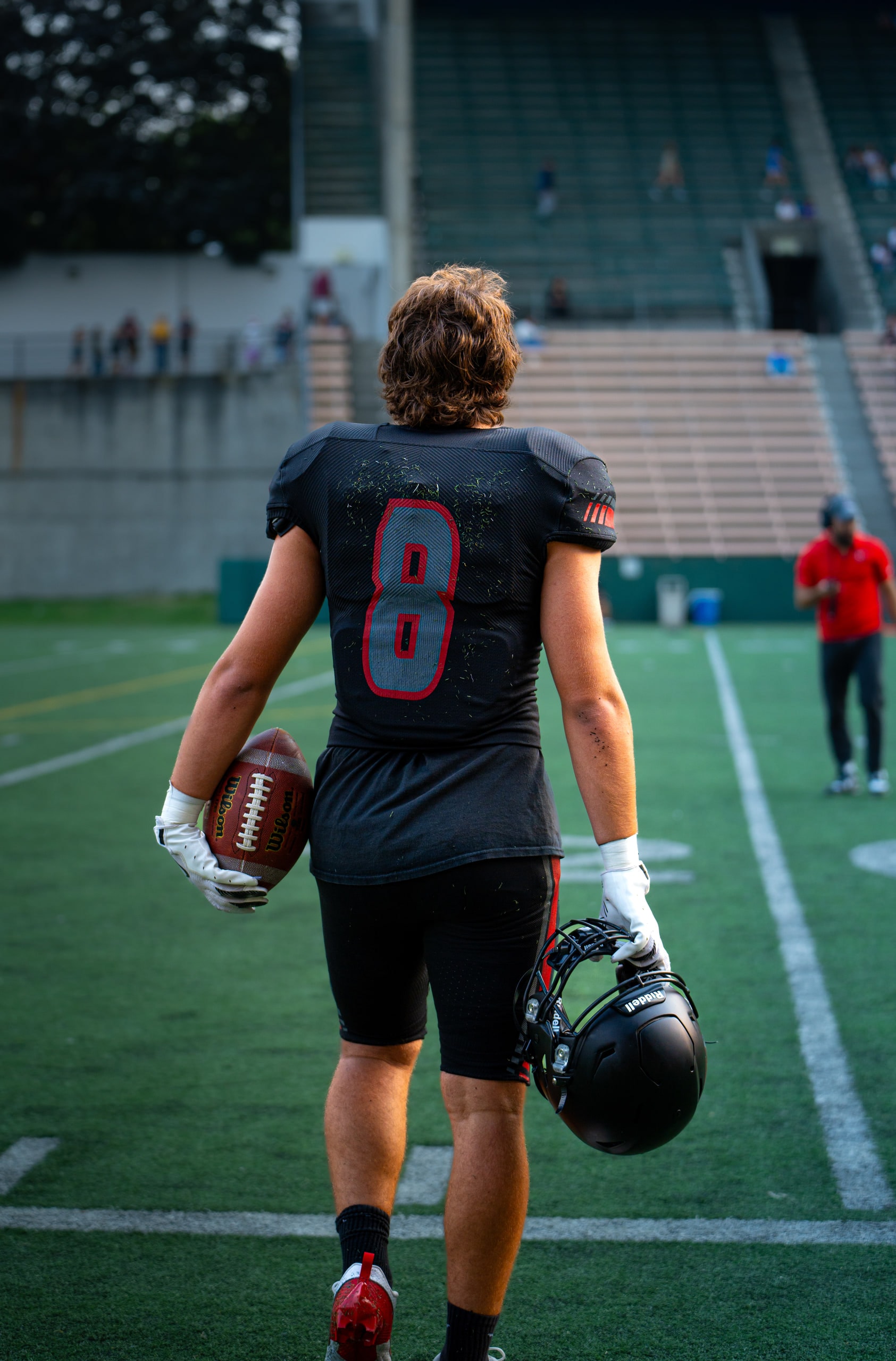 A football player in a black number 8 jersey carrying his ball and helmet off the field