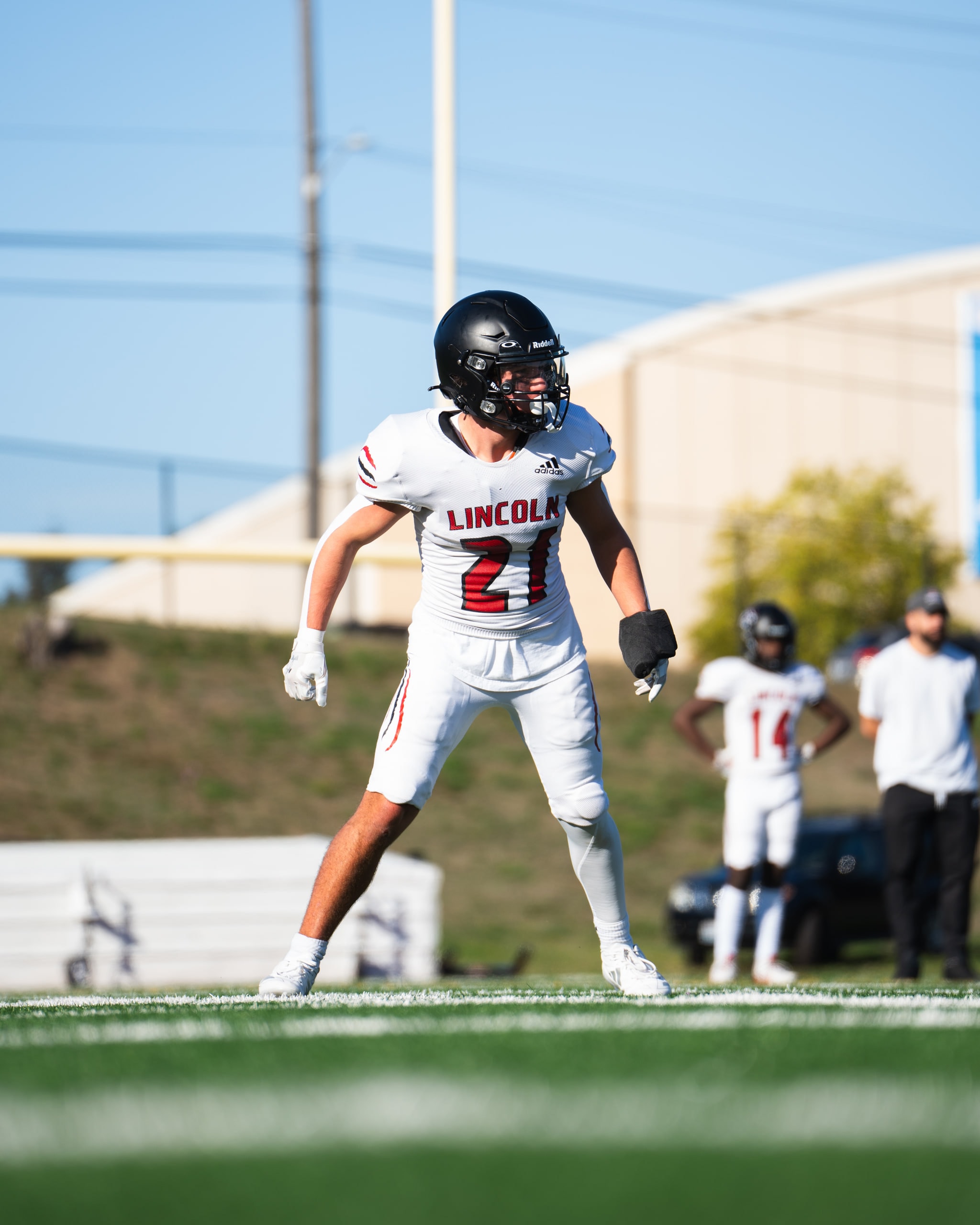 A defensive back in a white number 21 jersey set in his stance