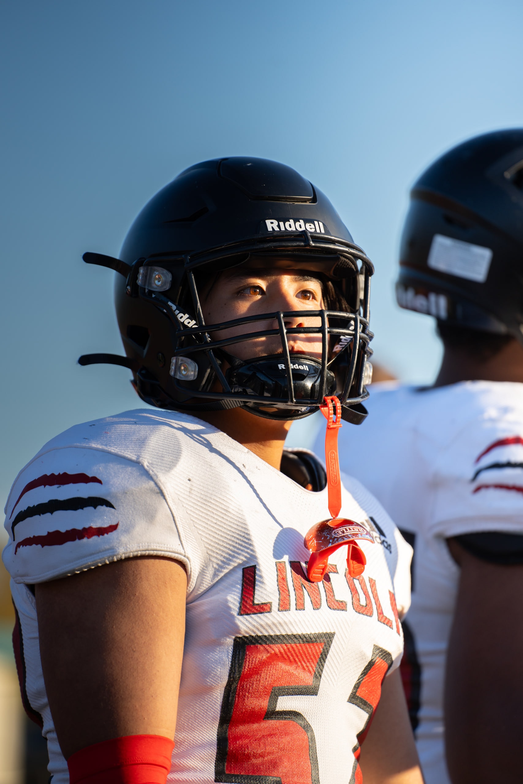 A helmeted player waiting on the sideline in late light